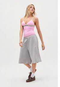 Rosa tettsittende topp med tynne stropper og svart midjebånd, kombinert med grå knelang shorts. Brune sko og hvite sokker fullfører antrekket.