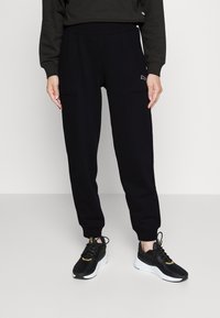 Pantaloni jogger neri con vestibilità rilassata, dotati di due tasche anteriori, vita elasticizzata e polsini a costine. Abbinati a sneakers nere.