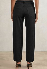 Pantalones anchos de mezclilla negra con cintura alta, dos bolsillos traseros y un dobladillo limpio. Llevados con sandalias de tacón alto negras con tiras.