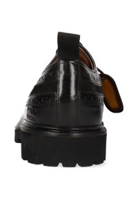 Zapato de cuero negro con detalles de brogue, puntera redondeada, tirador elástico y suela de goma negra gruesa. La vista trasera muestra un acabado pulido.