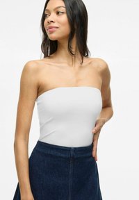 Top bianco senza spalline realizzato in un tessuto liscio ed elasticizzato, indossato con una gonna di jeans scura. Il top ha un design pulito e semplice, senza fantasie.