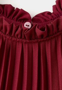Tissu plissé rouge profond avec bordure froncée assemblée et un petit bouton assorti cousu au bord central.