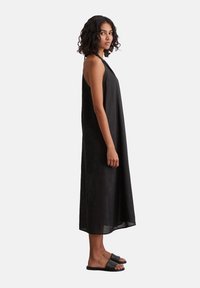 Schwarzes ärmelloses Kleid aus leichtem Stoff, mit einer lockeren Silhouette, die bis unter die Knie reicht, kombiniert mit flachen schwarzen Sandalen.