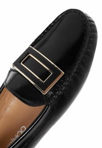 Mocassin en cuir noir avec une finition brillante, doté d'une boucle en métal rectangulaire et de coutures élaborées le long du bord. Intérieur lisse.