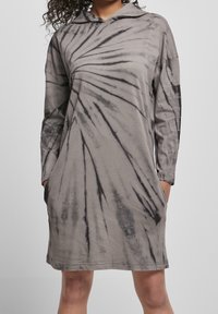 Szara sukienka w tie-dye z długim rękawem i kapturem, z czarnymi wirującymi wzorami, dwiema bocznymi kieszeniami oraz luźnym krojem. Miękka tekstura materiału.