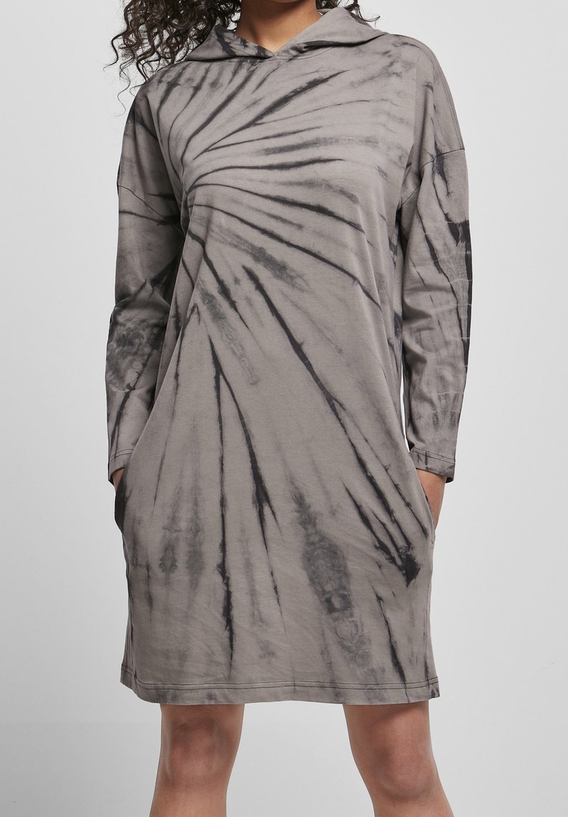 Szara sukienka w tie-dye z długim rękawem i kapturem, z czarnymi wirującymi wzorami, dwiema bocznymi kieszeniami oraz luźnym krojem. Miękka tekstura materiału.
