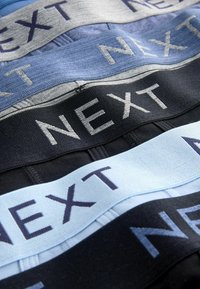 Cuatro cinturillas elásticas en varios colores: negro, azul oscuro, azul claro y gris, cada una con la palabra "NEXT" impresa en colores contrastantes.