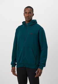 Teal zip-up hoodie with a front pocket, made of soft fabric, featuring a black Adidas logo on the chest and drawstring hood detail.