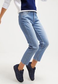 Ljusblå denimjeans med avslappnad passform, kort längd och subtila blekningar, kombinerat med mörkblå sneakers med en texturerad yta.