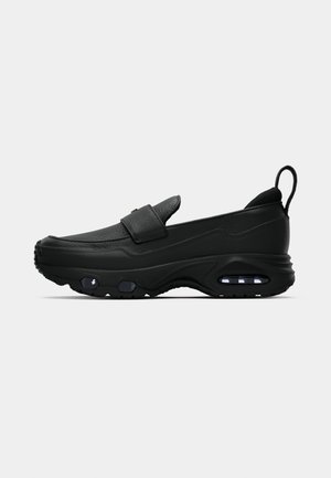 Sorte slip-on sko med tykk sål, luftdæmpning i hælen og forfoden, læderoverdel og trækflap bagpå.