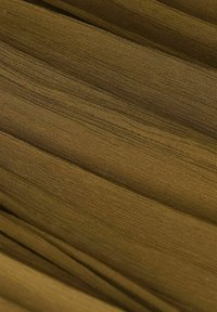 Tissu vert olive avec une surface douce et légèrement texturée, ponctuée de lignes fines et discrètes. Le matériau tombe doucement avec des plis superposés.