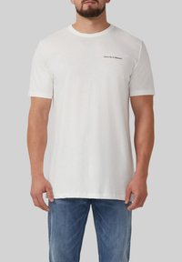 Witte katoenen t-shirt met korte mouwen, voorzien van een zwarte tekstafdruk met de tekst "Abonneer je op de Natuur" op de bovenste linkerkant.