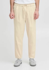 Beige bukser med elastisk talje og snøring, med en afslappet pasform og sidelæg, parret med lysegrå sportssko.