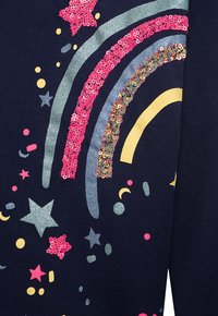 Marineblaues Sweatshirt mit einem Regenbogenmotiv, verziert mit glitzernden und paillettenbesetzten Akzenten in Pink, Gold sowie mehrfarbigen Sternen und Formen.