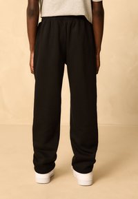 Black sweatpants with an elastic waistband, featuring a relaxed fit and cuffed ankle. Worn with white sneakers against a neutral backdrop.