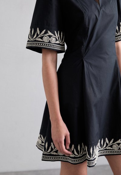 Vestido de algodón negro con mangas cortas, que presenta bordado floral blanco en los puños y el dobladillo. Textura suave, corsé ajustado y falda acampanada.