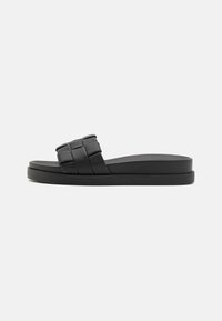 Black slide sandal with a woven strap design, flat rubber sole, and smooth texture. Minimalist shape with a low-profile silhouette.