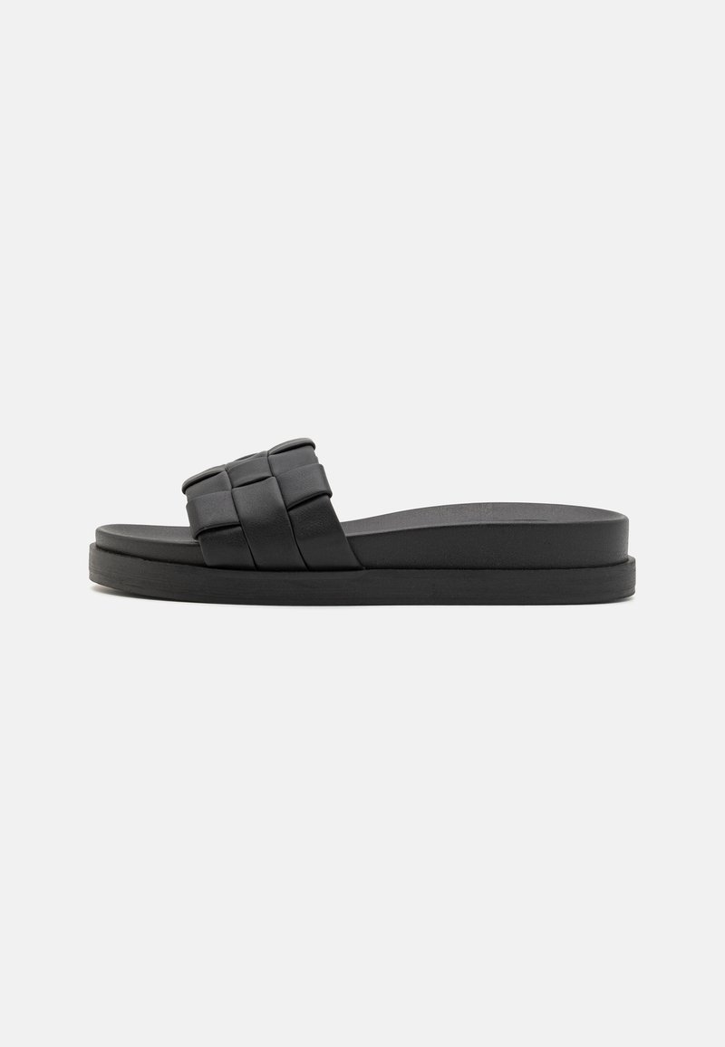 Black slide sandal with a woven strap design, flat rubber sole, and smooth texture. Minimalist shape with a low-profile silhouette.