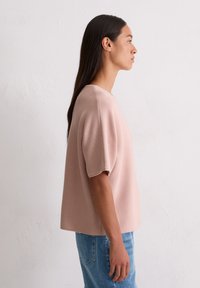 Jasnoróżowa, krótkosłodkowa bluzka dzianinowa o pudełkowym kroju, teksturowany materiał i okrągły dekolt, w parze z niebieskimi dżinsami.