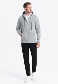 Haut à capuche gris zippé avec un capuchon, cordon de serrage et poches avant, associé à un pantalon à carreaux noirs et des baskets blanches.