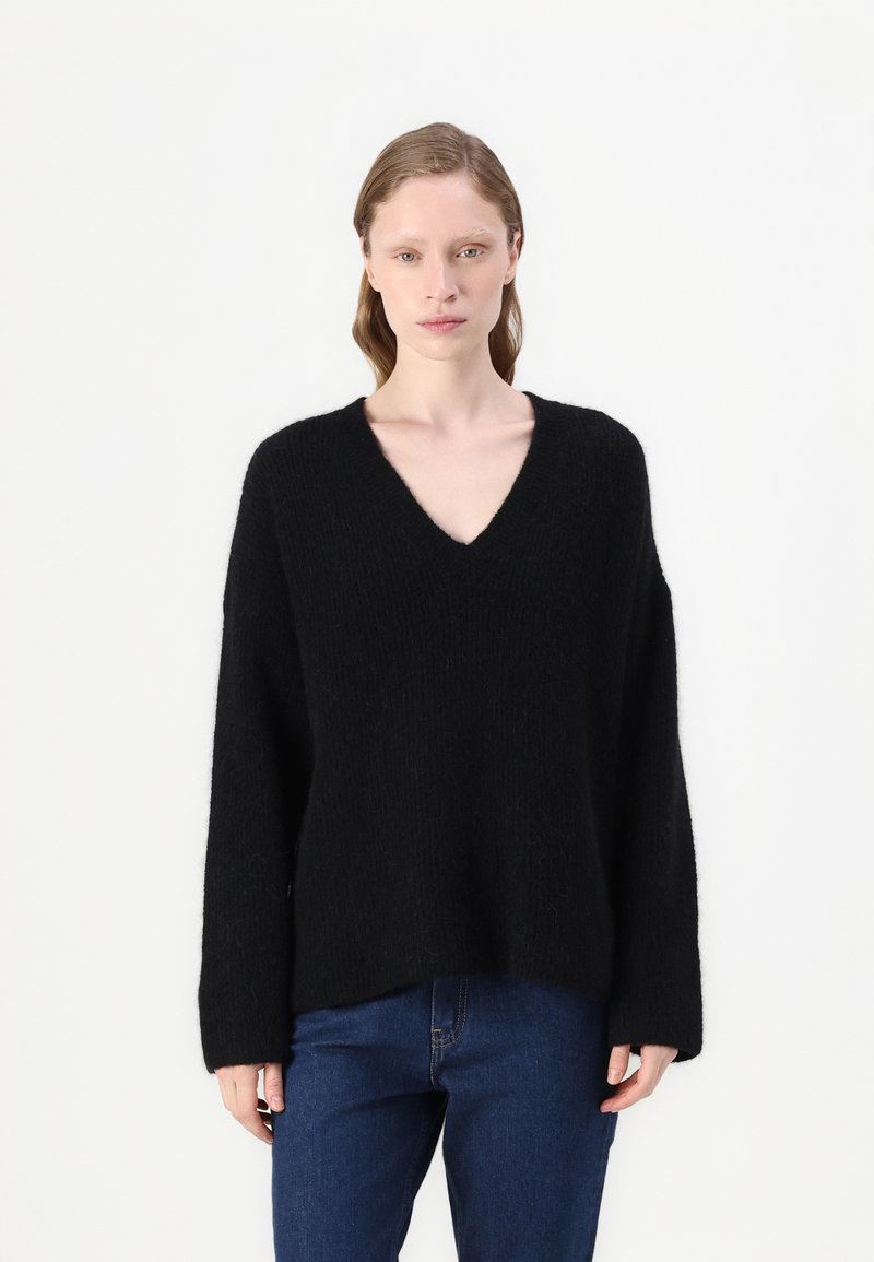 Pulover negru tricotat cu decolteu în V, croi lejer și mâneci lungi. Textură moale, design minimalist, asortat cu blugi denim albastri.