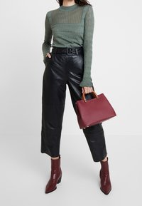 Světle zelený pletený svetr se strukturovanými vzory, černé kožené kalhoty, bordó kabelka s dřevěnými madly a odpovídající kotníkové boty.