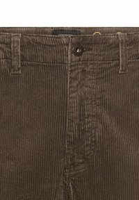 Brune kordfløjsbukser med lodrette ribber, metalknaplukning og forlommer. Stoffet har en blød tekstur.