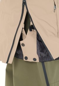 Beige isolerad jacka med svart dragkedja, marinblå inredning och tryckknapps-stängning. Synlig sömnad och strukturerad tygdetalj.