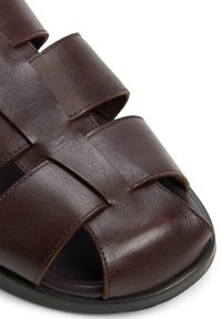 Braune Ledersandale mit einem offenen Zehendesign, kreuzenden Riemen und einer glatten Textur, ruhend auf einer schwarzen Sohle.
