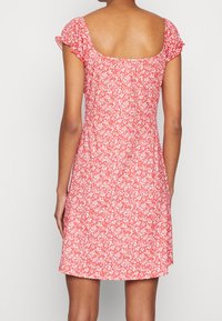 Czerwona sukienka w kwiaty z kwadratowym dekoltem, krótkimi falbanastymi rękawami i dopasowaną górą, z delikatnym białym wzorem kwiatowym na całej powierzchni.