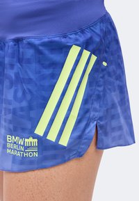 Μπλε σορτς για τρέξιμο με κίτρινες ρίγες Adidas και λογότυπο BMW Berlin Marathon, φορεμένα στο πάνω μέρος του μηρού ενός ατόμου.
