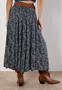 Navy blue, pleated maxi skirt with a white abstract pattern, featuring an elastic waistband and a brown woven belt accent.