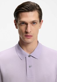 Lawendowa koszulka polo z teksturowanej tkaniny z klasycznym kołnierzykiem i dwoma guzikami. Na piersi znajduje się małe haftowane logo „BOSS”.