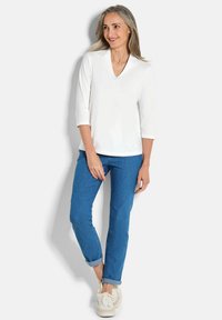 Witte v-hals top met driekwart mouwen, gecombineerd met blauwe jeans en witte sneakers. Gladde textuur, casual pasvorm en opgerolde boorden op de broek.