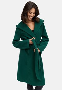 Green wool blend coat with a wide collar, long sleeves, waist tie, and side pockets. The fabric has a smooth, soft texture.