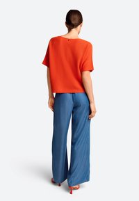 Rode, korte mouwen trui met een cropped ontwerp; de achterkant heeft een subtiel knoopdetail. Gecombineerd met losse blauwe denim broeken en rode hakken.