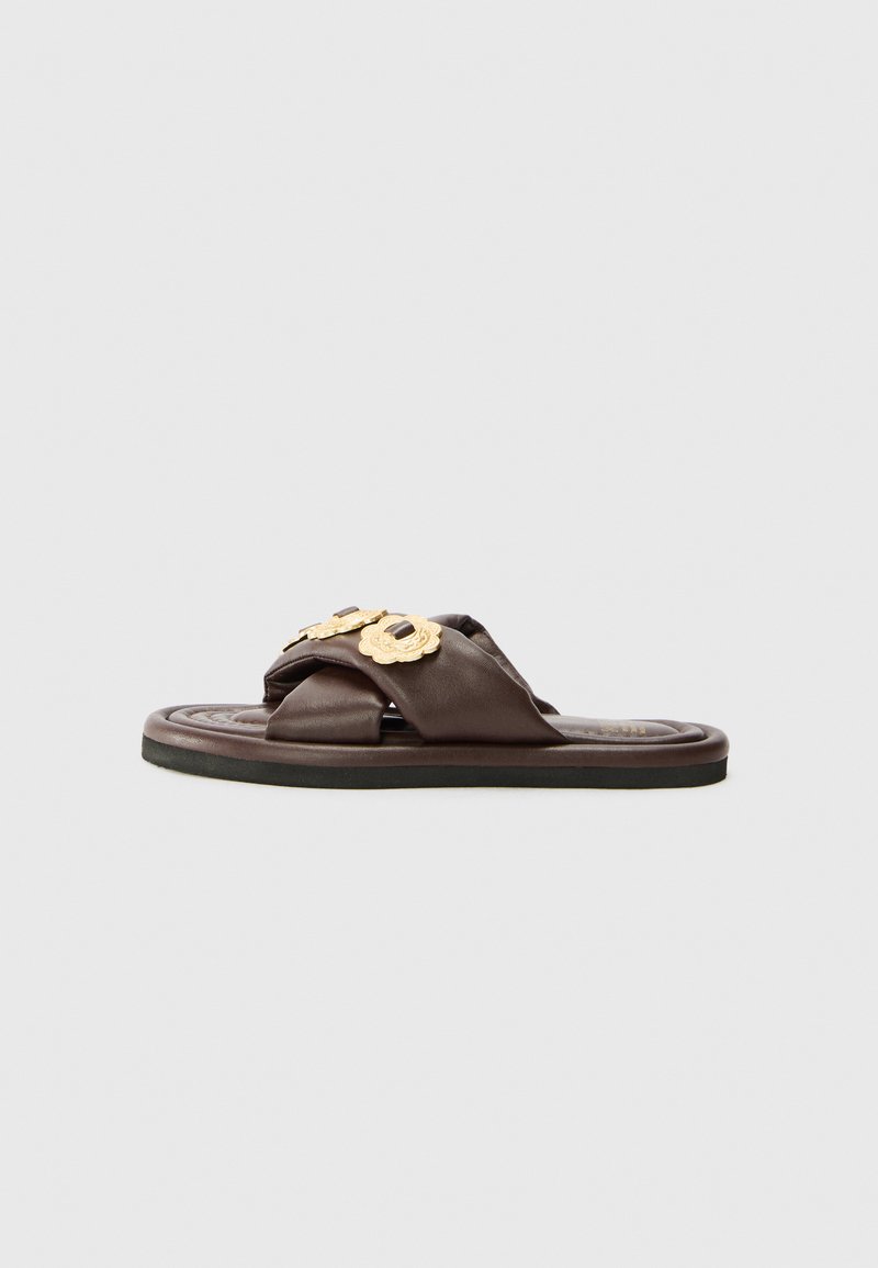 Brown leather slide sandal with decorative gold hardware, crisscross design, and a textured footbed, featuring a flat black sole.