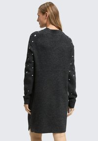 Dunkelgraues Strickkleid mit rundem Halsausschnitt, langen Ärmeln und weißen herzförmigen Akzenten an den Schultern. Weiche Stricktextur.