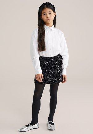 Balta pogtota krekliņa ar izšūtu apkakli, melna pērļota mini svārki, melnas zeķbikses un sudraba baleta kurpes. Vienkāršs un elegants dizains.