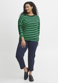 Zelena in črna prostrana dolgem rokavu s pasom, v kombinaciji z mornarsko modrimi kratkimi hlačami. Črne čevlje brez zavezovanja. Mehka tkanina z ohlapnim krojem.