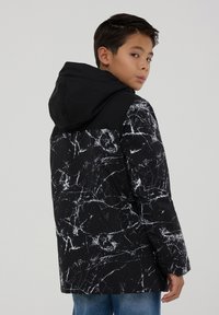 Giacca nera con motivo marmoreo bianco, cappuccio e maniche lunghe. Presenta un design testurizzato, vestibilità informale e tasche frontali.