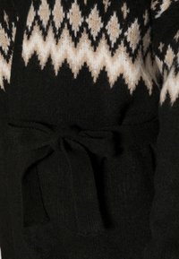 Černý pletený cardigan s texturovaným povrchem, s krémovým a hnědým geometrickým vzorem na vršku a zavázaným opaskem v pase.