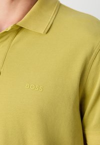 Polo de couleur jaune clair, fabriqué en tissu texturé. Doté d'un col classique et du logo "BOSS" en relief sur la poitrine.