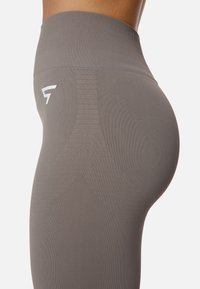 Leggings grigi a vita alta realizzati in un tessuto elasticizzato, con una sottile texture a costine e un logo bianco sul lato.