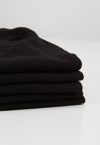 Calze nere lavorate a maglia impilate ordinatamente con una consistenza morbida. Ogni calza presenta un design e una forma costanti, mostrando cuciture uniformi in tutto il capo.