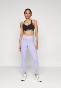 Zwarte sportbeha met logoband, gecombineerd met lichtpaarse hoge taille legging met een contrasterende logoriem. Witte sportschoenen.
