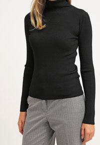 Svart ribbad turtlenecktröja med långa ärmar. Har en åtsittande design och mjuk textur, ihop med ljusgrå randiga byxor.