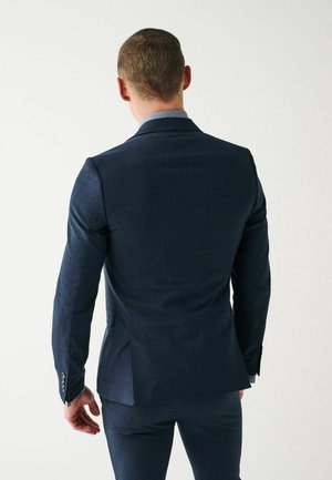 Giacca da abito a quadri blu navy con finitura satinata, caratterizzata da risvolti a punte, uno spacco singolo e polsini con bottoni. Vestibilità su misura.