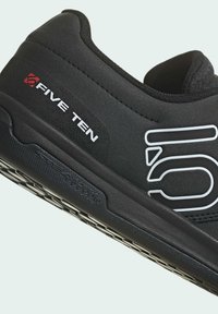 Sneaker nera con tomaia testurizzata, caratterizzata da un logo "Five Ten" bianco e rosso, e suola in gomma con grip a motivo per aderenza.