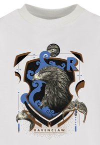 White t-shirt featuring a Ravenclaw crest with a detailed eagle graphic, blue and brown accents, swirling patterns, and character icons.